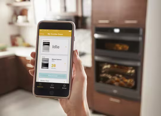 Person using the Whirlpool app on a smartphone to remotely control the WOED5027LB double wall oven.