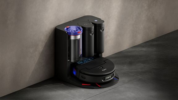 Dyson Spot+Scrub Ai robot vacuum cleaner shown on a hard floor surface next to its hygienic cyclonic docking station.