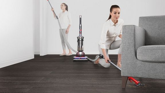 Woman using Dyson Ball Animal 3 vacuum under a sofa; second view shows same vacuum used upright with hose attachment for high reach cleaning on hardwood floors.