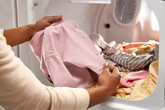 Freshly dried wrinkle-free clothes being removed from a Whirlpool dryer drum.
